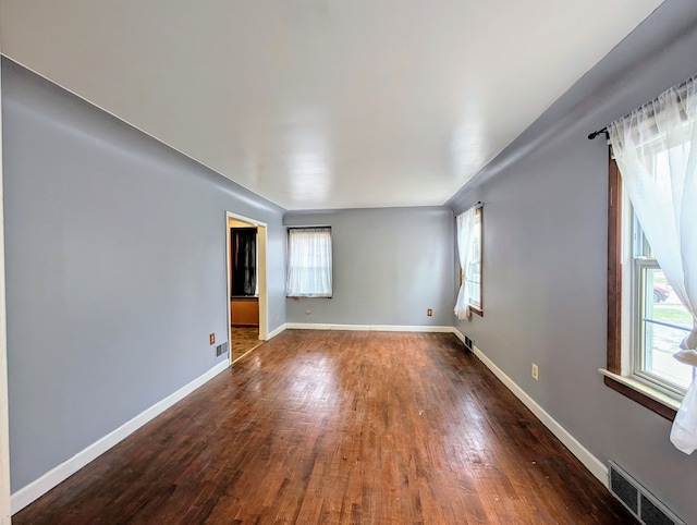 spare room with dark wood-type flooring, visible vents, and plenty of natural light