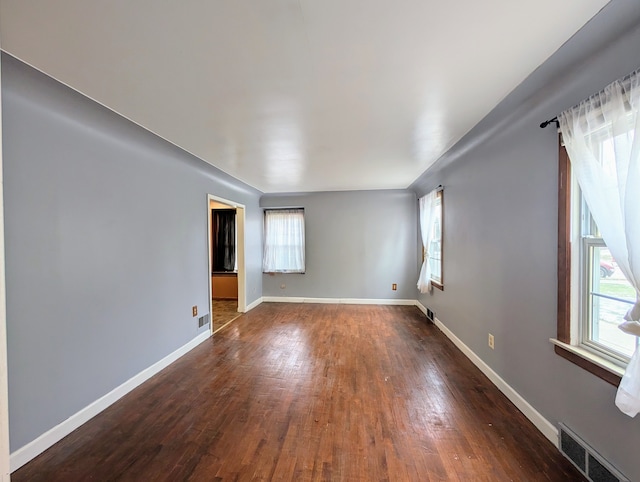 unfurnished room with a wealth of natural light, dark wood-style flooring, and visible vents