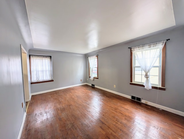 empty room featuring dark wood-style flooring, visible vents, and baseboards