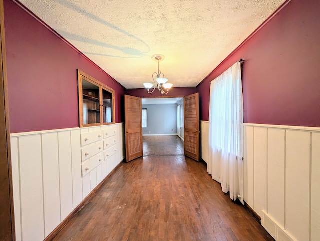 unfurnished dining area featuring dark wood-type flooring, wainscoting, a textured ceiling, and an inviting chandelier