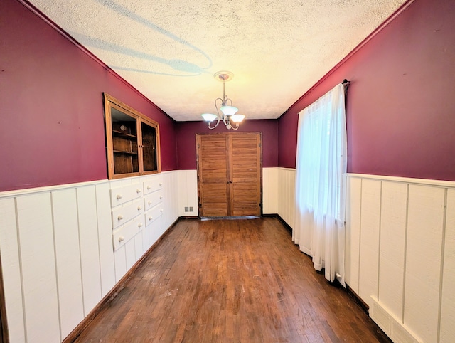 unfurnished dining area with dark wood-style floors, a notable chandelier, visible vents, wainscoting, and a textured ceiling