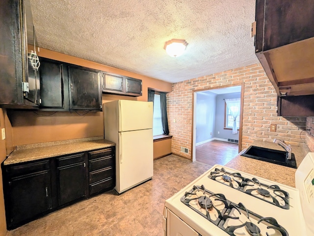 kitchen with white appliances, brick wall, light countertops, a textured ceiling, and a sink