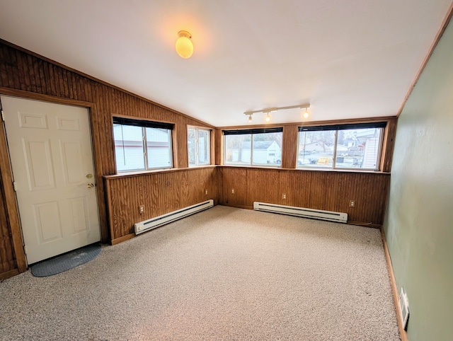 carpeted spare room with a baseboard heating unit, vaulted ceiling, wood walls, and track lighting