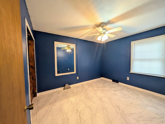 spare room with a textured ceiling, a ceiling fan, visible vents, and baseboards