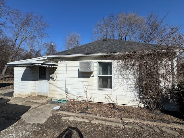 back of house featuring a shingled roof and a wall mounted air conditioner