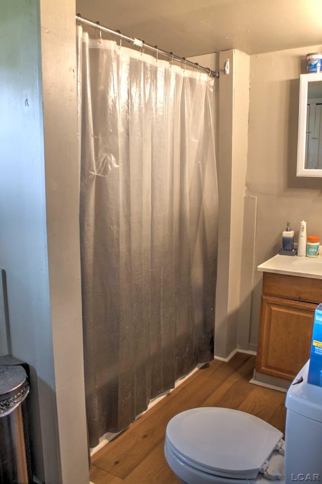 bathroom featuring toilet, curtained shower, wood finished floors, and vanity