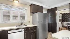 kitchen with light countertops, freestanding refrigerator, white dishwasher, a sink, and dark brown cabinets