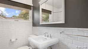 half bathroom featuring a wainscoted wall, toilet, a sink, and tile walls