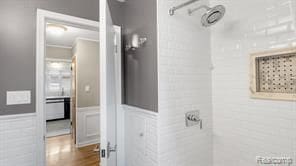 bathroom with ornamental molding, wainscoting, a tile shower, and wood finished floors