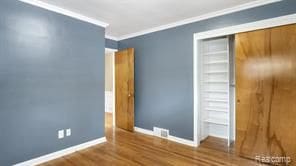 unfurnished bedroom with baseboards, visible vents, ornamental molding, wood finished floors, and a closet