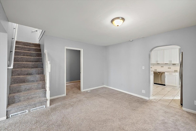 interior space with light carpet, visible vents, arched walkways, baseboards, and stairway