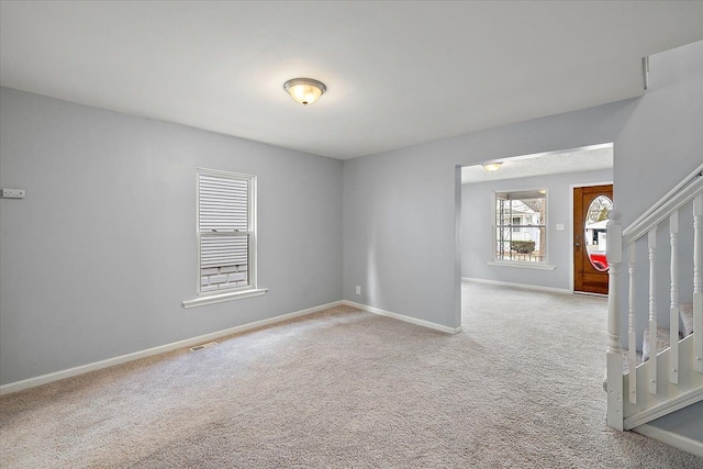 empty room featuring carpet floors, baseboards, and stairway