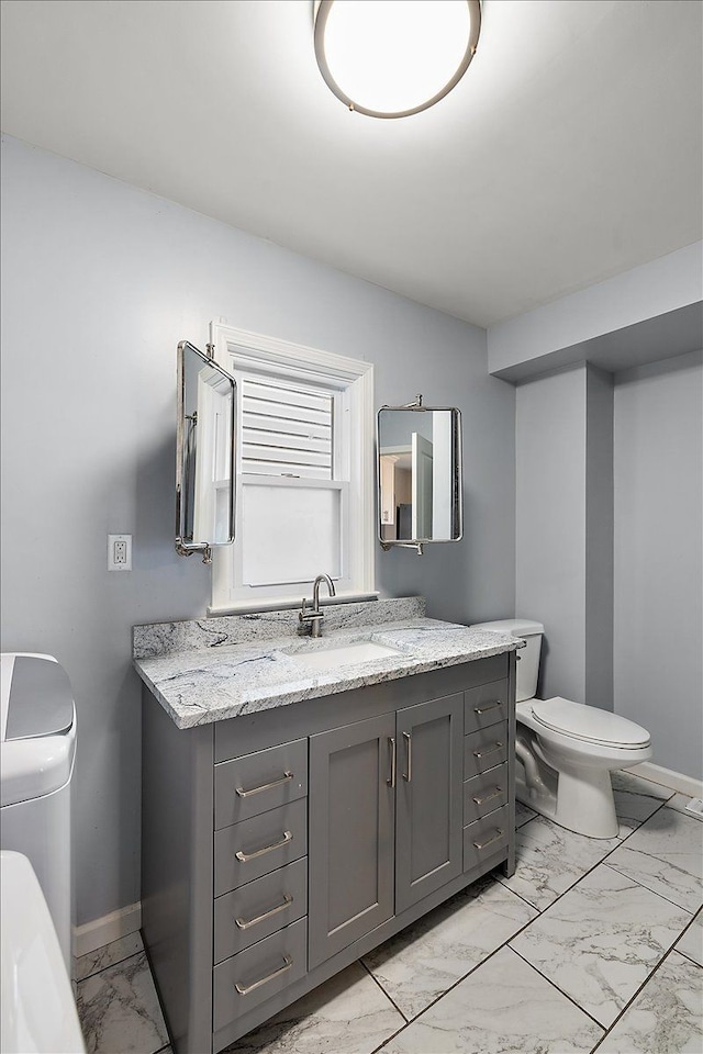 half bath with toilet, marble finish floor, baseboards, and vanity