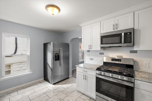 kitchen with arched walkways, marble finish floor, stainless steel appliances, backsplash, and white cabinets