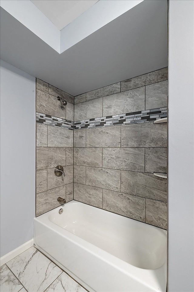 bathroom featuring marble finish floor, baseboards, and bathtub / shower combination