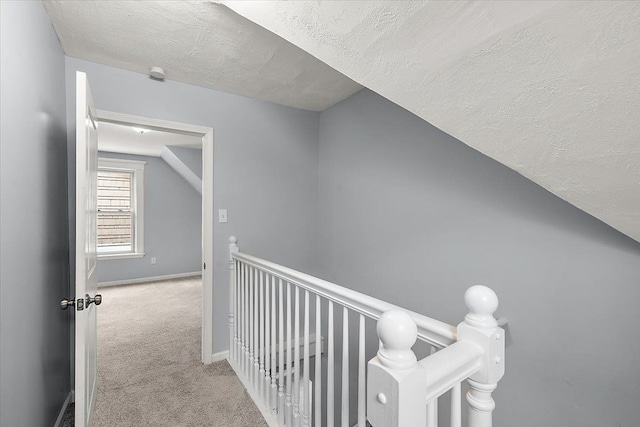 hallway featuring baseboards, lofted ceiling, a textured ceiling, an upstairs landing, and carpet floors