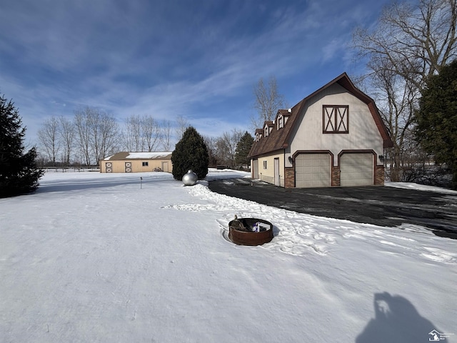 yard covered in snow featuring a barn, driveway, a garage, a fire pit, and an outdoor structure