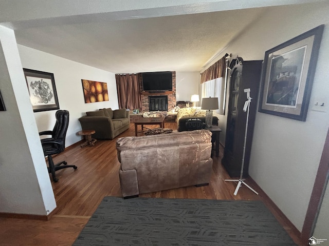 living room featuring a textured ceiling, a fireplace, baseboards, and wood finished floors