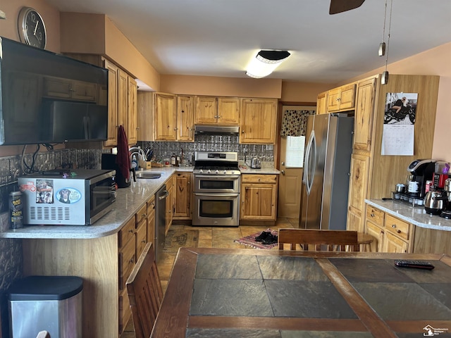 kitchen with decorative backsplash, stainless steel appliances, stone tile flooring, under cabinet range hood, and a sink