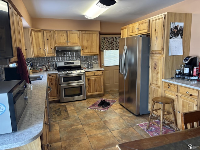 kitchen with a sink, under cabinet range hood, appliances with stainless steel finishes, and backsplash