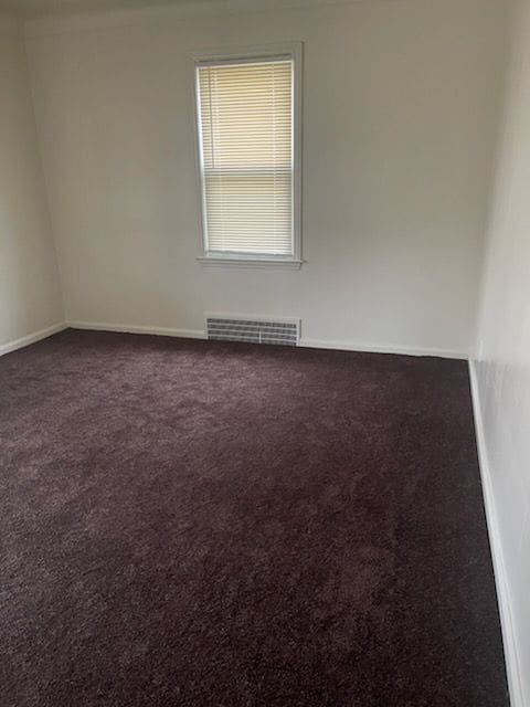 spare room with visible vents, dark carpet, and baseboards