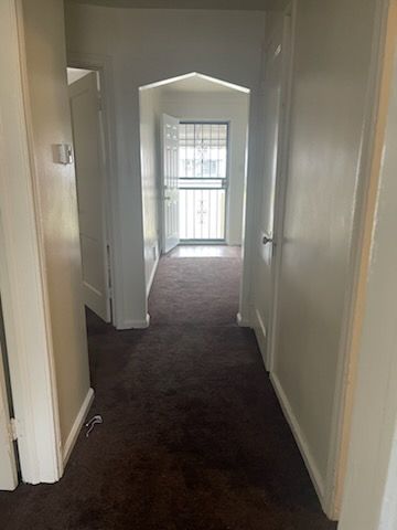 corridor with baseboards and dark carpet