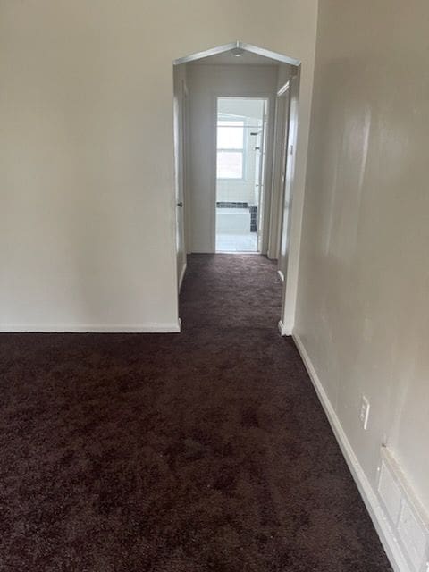 corridor with visible vents, dark carpet, and baseboards