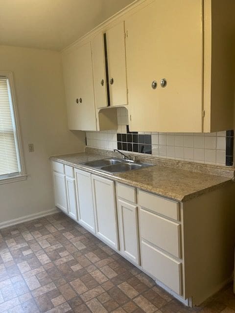 kitchen with a sink, white cabinetry, baseboards, light countertops, and tasteful backsplash