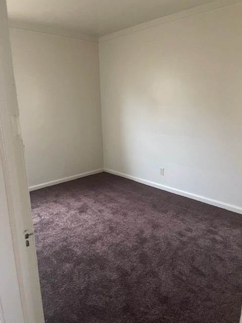 empty room with crown molding, dark carpet, and baseboards