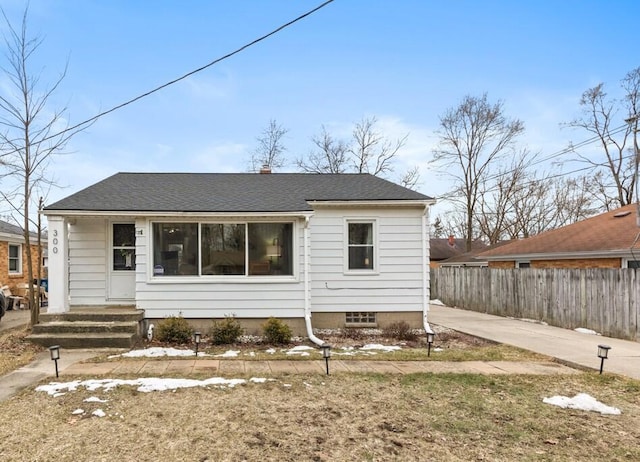 bungalow-style home with a shingled roof and fence