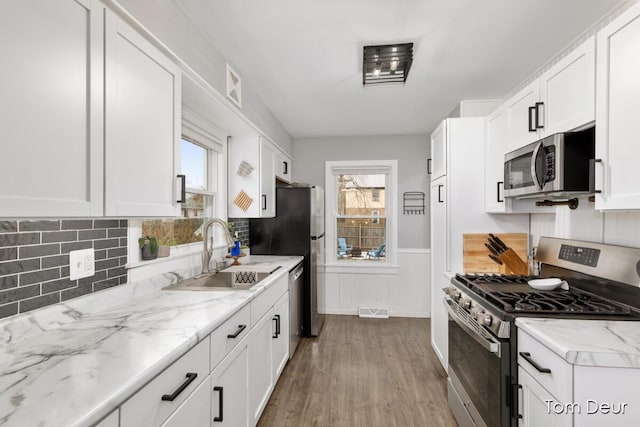 kitchen with a wainscoted wall, visible vents, appliances with stainless steel finishes, white cabinets, and a sink