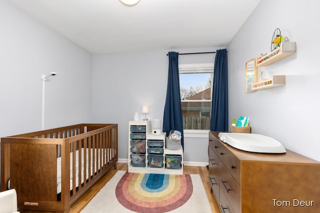 bedroom with a crib, baseboards, and wood finished floors