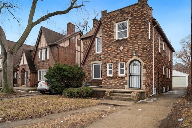 english style home with a garage, an outbuilding, brick siding, and a chimney