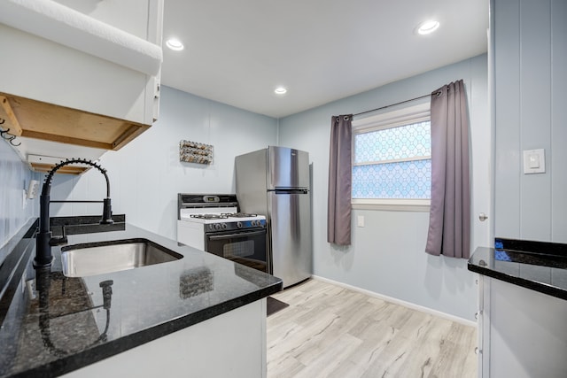 kitchen featuring white cabinets, range with gas cooktop, freestanding refrigerator, light wood-style floors, and a sink