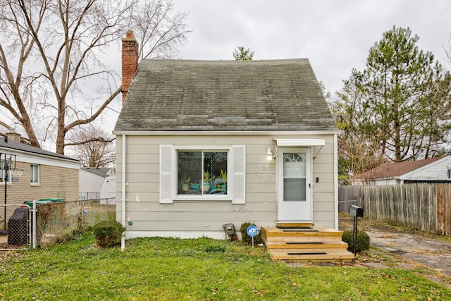 view of front of house featuring entry steps, a fenced backyard, a shingled roof, a front lawn, and a chimney