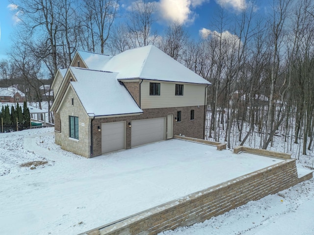 view of snow covered exterior featuring a garage and brick siding