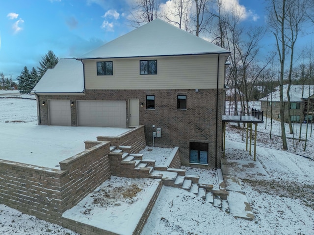 snow covered rear of property with brick siding and a garage