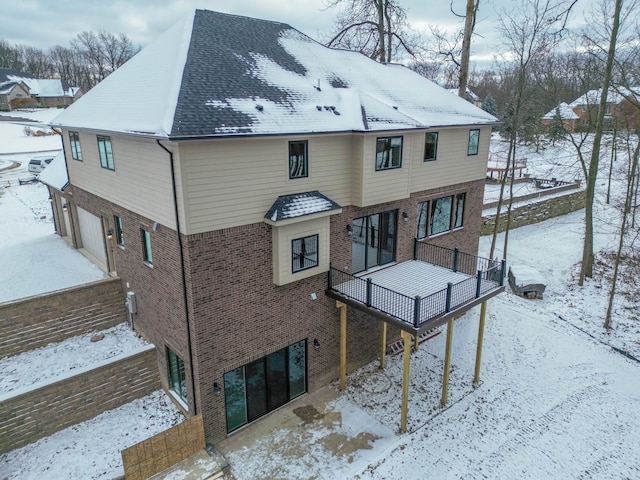 snow covered property with brick siding, a deck, and a garage