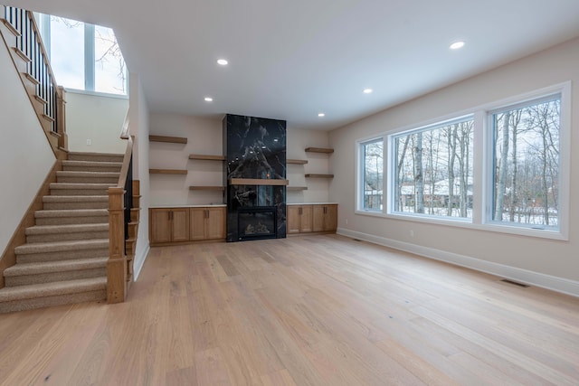 unfurnished living room with stairway, plenty of natural light, visible vents, and light wood finished floors