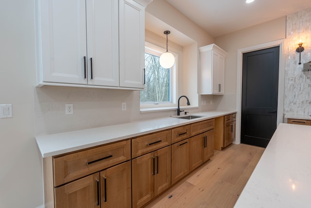 kitchen with pendant lighting, light wood-type flooring, light countertops, white cabinets, and a sink