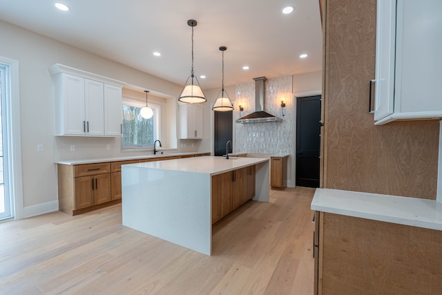 kitchen featuring light wood finished floors, a sink, recessed lighting, wall chimney exhaust hood, and a kitchen island with sink