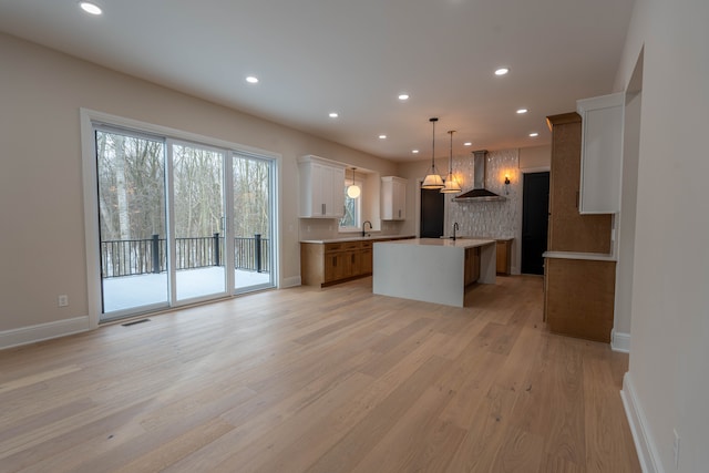 kitchen with a sink, light wood-style floors, wall chimney exhaust hood, and recessed lighting