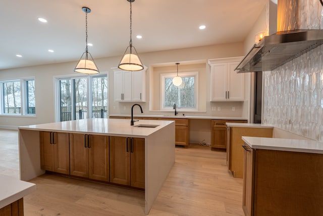 kitchen featuring ventilation hood, an island with sink, light wood-style floors, and a sink