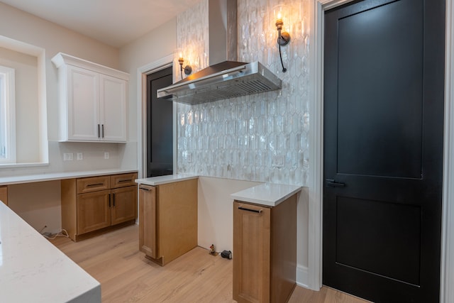 kitchen with light wood-type flooring, light countertops, and wall chimney range hood