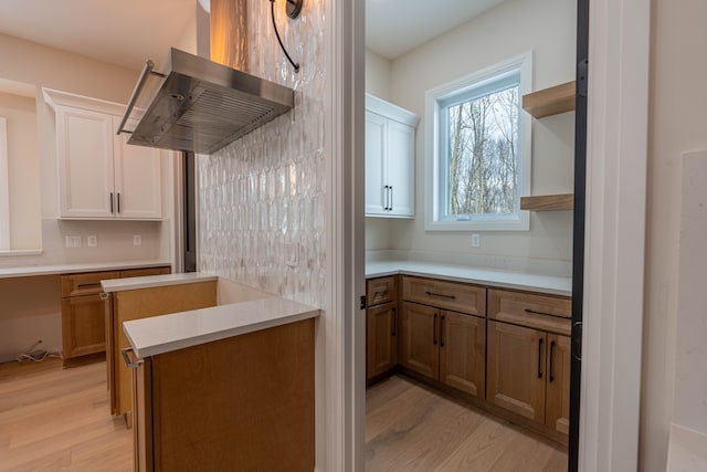 kitchen featuring open shelves, wall chimney exhaust hood, light wood-style floors, and light countertops