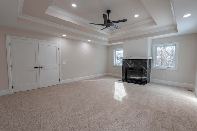 unfurnished living room with light colored carpet, a ceiling fan, and a tray ceiling