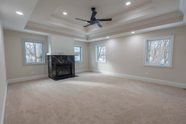 unfurnished living room featuring a tray ceiling, ornamental molding, baseboards, and light carpet