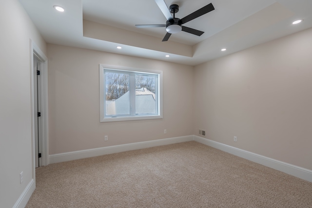 spare room with a tray ceiling, recessed lighting, carpet, and visible vents