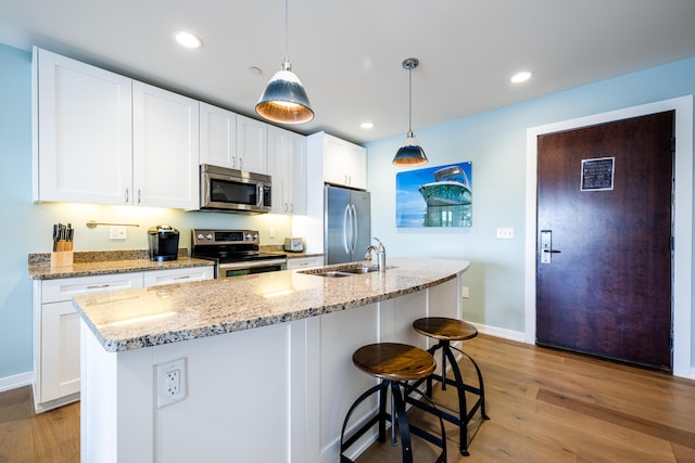 kitchen with appliances with stainless steel finishes, white cabinets, a sink, and light wood-style flooring