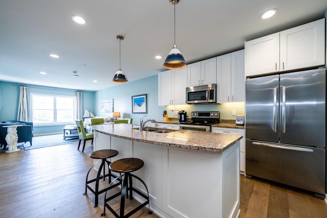 kitchen with appliances with stainless steel finishes, white cabinetry, a sink, and hardwood / wood-style flooring